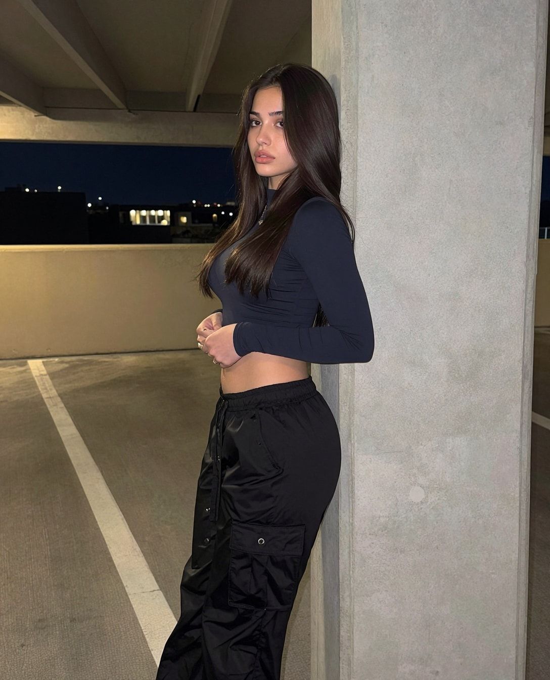 AI character in a parking garage at night, navy crop top and black cargo pants.